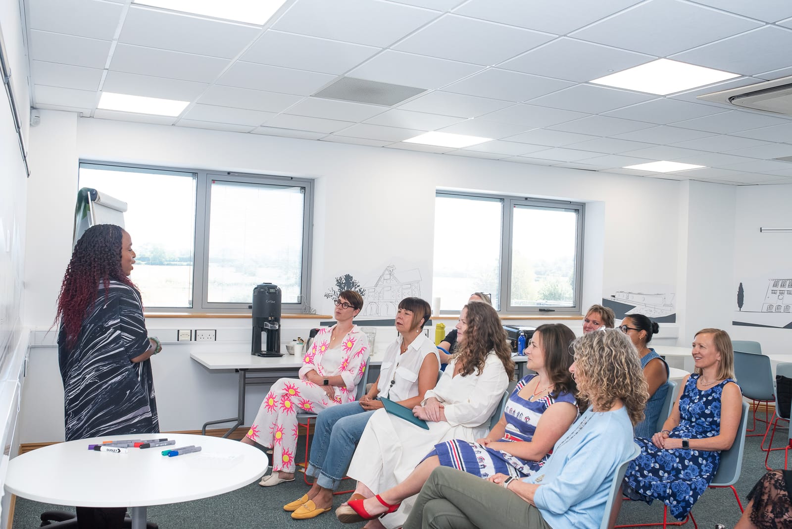 Facilitator at a whiteboard leading a group of ten delegates seated in a bright modern training room.